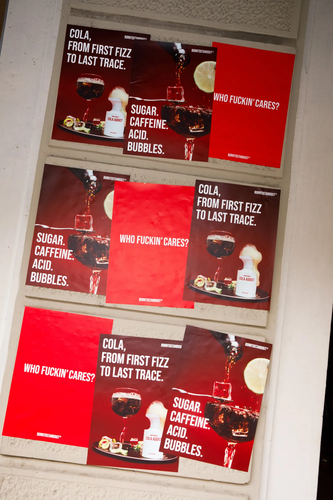 Manifesti della campagna BORNTOSTANDOUT Cola Addict affissi su un muro, con immagini di cola versata nel bicchiere e claim "Sugar. Caffeine. Acid. Bubbles." / BORNTOSTANDOUT Cola Addict campaign posters pasted on a wall, showing cola being poured into a glass alongside the claim "Sugar. Caffeine. Acid. Bubbles."